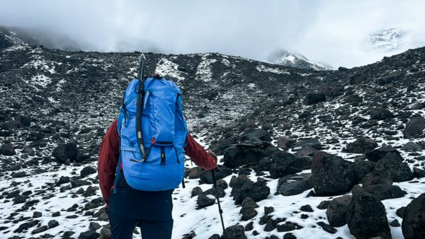 A hiker with a blue backpack navigates the rocky, snow-covered terrain of Chimborazo Volcano in Ecuador.