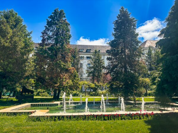 Fountains and vibrant greenery create a serene atmosphere in English Park, Craiova, Romania, framed by tall trees and a sunny sky.