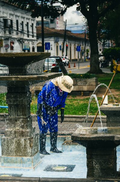 Colorful fountain in Parque La Merced with a person in blue attire examining the water, surrounded by lush greenery in Ibarra, Ecuador.
