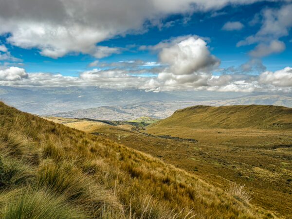 Lush grasslands and rolling hills under a blue sky with clouds, overlooking the breathtaking landscape of Pichincha, Ecuador.