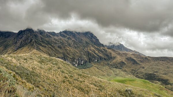Majestic Ruminahui volcano towers over green valleys under a dramatic, cloudy sky in Ecuador's highlands.
