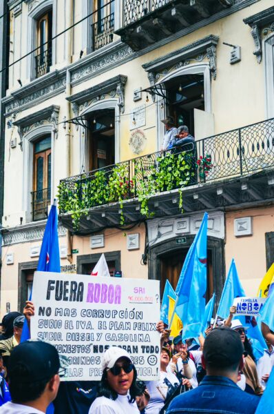 Colorful International Workers' Day parade in Quito, Ecuador, featuring protesters with flags and signs in front of a historic building.