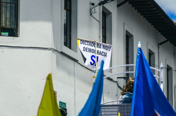 Colorful flags and banners adorn a street during the International Workers' Day parade in Quito, Ecuador, with a sign advocating democracy.