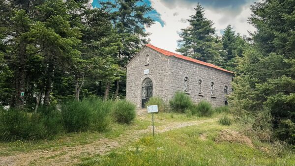 Old stone church framed by lush greenery along the path to Valtesiniko, Arcadia, Greece. The building features a red-tiled roof.