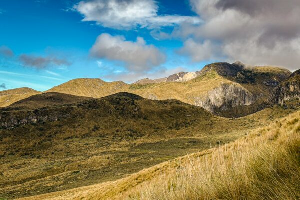 Golden grasses and rocky slopes under a blue sky with clouds at Pichincha Volcano in Ecuador. Scenic mountain landscape unfolds.