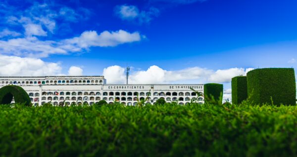 Tulcan Cemetery features lush green hedges against a backdrop of white architectural elements and a vibrant blue sky in Ecuador.
