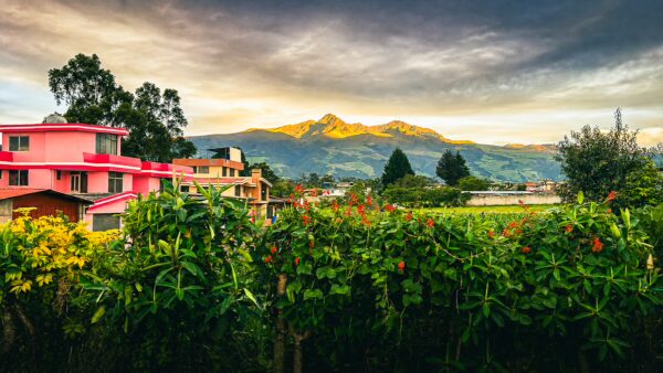 Ruminahui Volcano looms over vibrant greenery and colorful homes in Machachi, Ecuador at sunset.