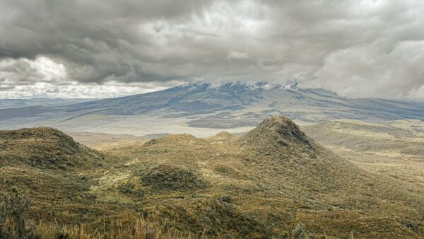 Dramatic cloud coverage over lush green hills with the volcanic peaks of Ruminahui in the background, Ecuador.