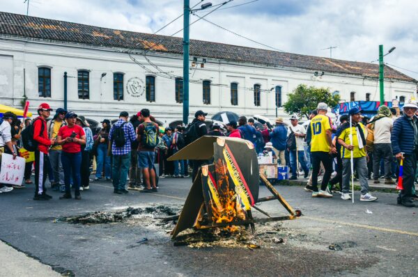 Crowds gather for the International Workers' Day parade in Quito, Ecuador, with a burning barricade in the foreground.