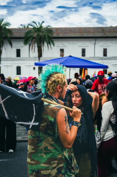 International Workers' Day parade in Quito, Ecuador, featuring colorful outfits, flags, and a lively crowd under a cloudy sky.