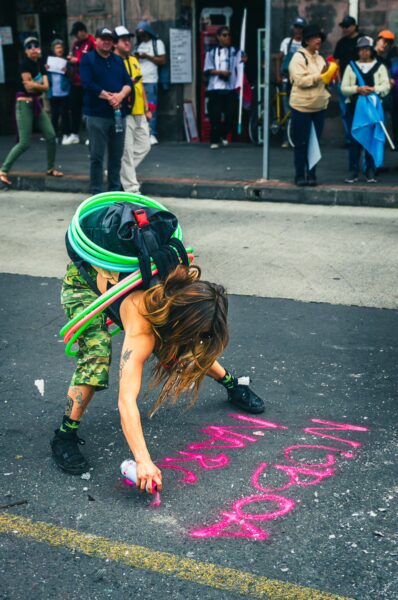 Vibrant scene from the International Workers' Day parade in Quito, Ecuador, featuring a person spray-painting a colorful message on the street.
