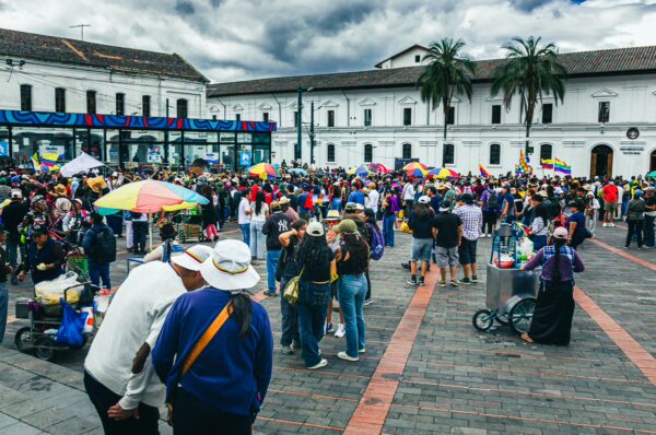 Vibrant crowd celebrating International Workers' Day in Quito, Ecuador, with colorful umbrellas and historic buildings in the background.