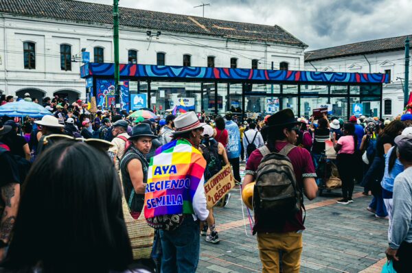 Crowd celebrating International Workers' Day in Quito, Ecuador, with vibrant banners and traditional attire under a cloudy sky.