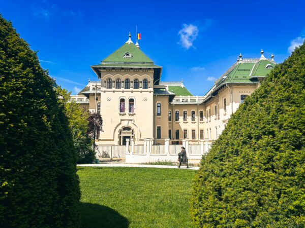 Administrative Palace of Craiova in Romania features a grand architectural design surrounded by lush greenery and clear blue skies.