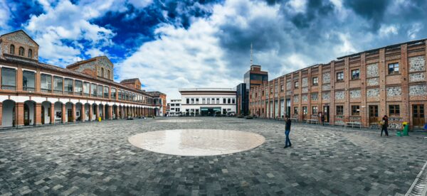 Centro Cultural El Cuartel in Ibarra, Ecuador features a spacious courtyard with stone paving and surrounding historic buildings under an expansive sky.