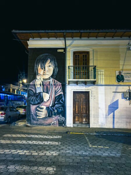 Vibrant street mural of a child on a building in Machachi, Ecuador, showcasing detailed artwork against a night backdrop.