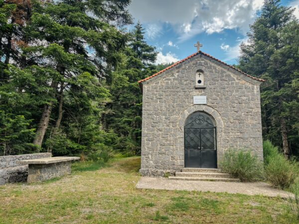 Charming stone chapel nestled among lush greenery in Magouliana, with a serene atmosphere and a clear blue sky.
