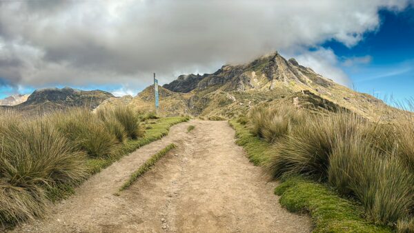Expansive view of Pichincha Volcano, Ecuador, featuring a winding dirt path and lush surrounding grasslands under a dramatic sky.