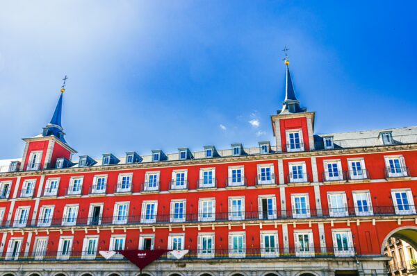 Vibrant red buildings with blue spires in Plaza Mayor, Madrid, against a clear sky, showcasing iconic Spanish architecture.