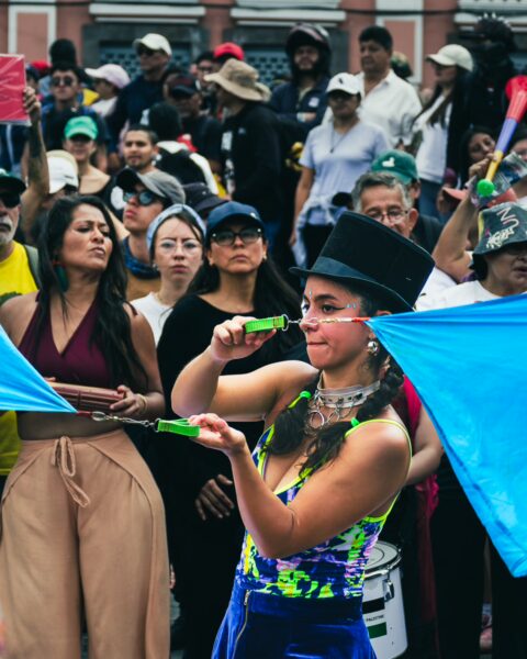 Vibrant scene from the International Workers' Day parade in Quito, Ecuador, showcasing a performer with blue flags and a lively crowd.