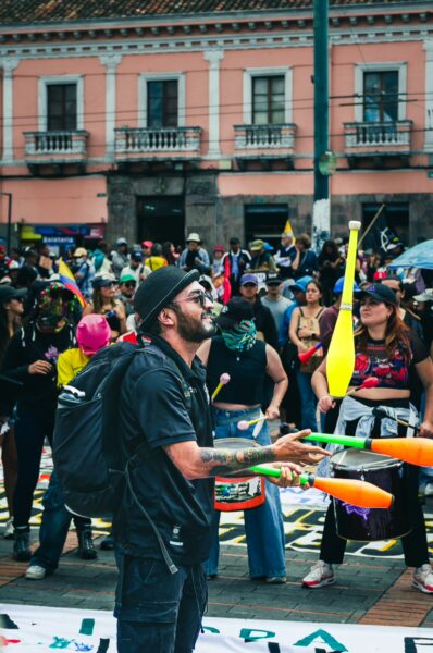 Juggler performing at the International Workers' Day parade in Quito, Ecuador, surrounded by a vibrant crowd and colorful banners.