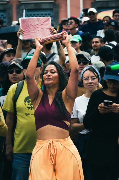 Celebrating International Workers' Day, a woman raises a banner amidst a lively crowd in Quito, Ecuador.