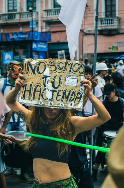 Colorful crowd at the International Workers Day parade in Quito, Ecuador, featuring a protester holding a sign with a message.