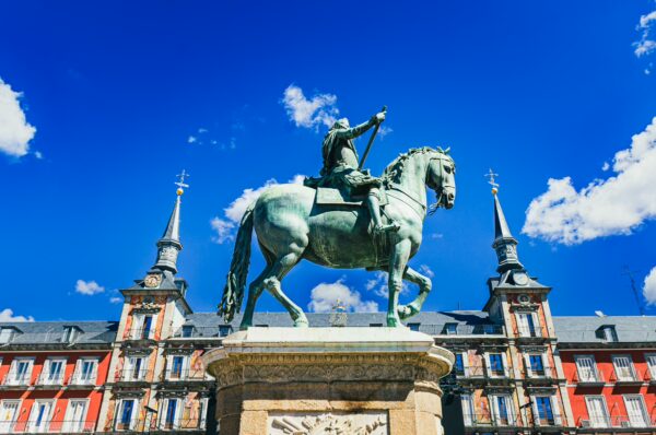 Statue of Felipe III on horseback against a bright blue sky, set in the vibrant Plaza Mayor, Madrid, Spain.