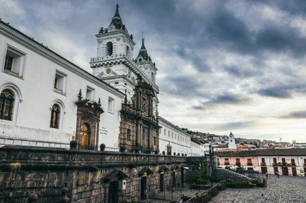 Colonial architecture stands majestically at San Francisco Square, Quito, Ecuador, under a dramatic cloudy sky.