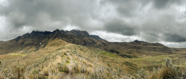 Lush green hills and rugged mountains under a cloudy sky near Volcán Ruminahui, Ecuador, showcase stunning natural beauty.