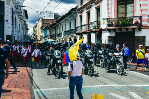 Colorful crowd celebrating International Workers' Day with motorcycles lined up in Quito, Ecuador, under a cloudy sky.