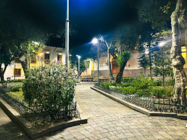 Lush greenery and illuminated walkways create a serene atmosphere in Plaza San Marcos, Quito, Ecuador, at night.