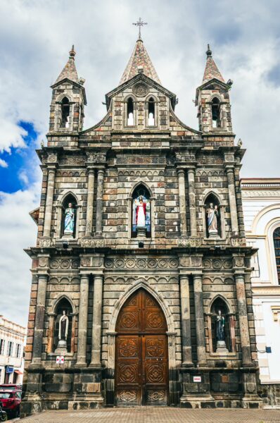 Capilla Episcopal features ornate stone architecture and tall spires, set against a cloudy sky in Ibarra, Ecuador.