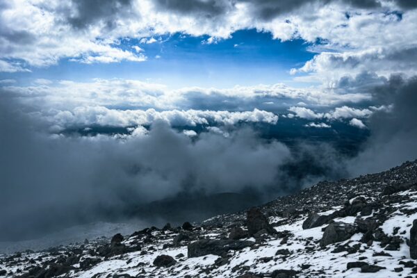 Majestic Chimborazo volcano looms above a dramatic cloudscape, with rocky terrain and patches of snow contrasting against the sky in Ecuador.
