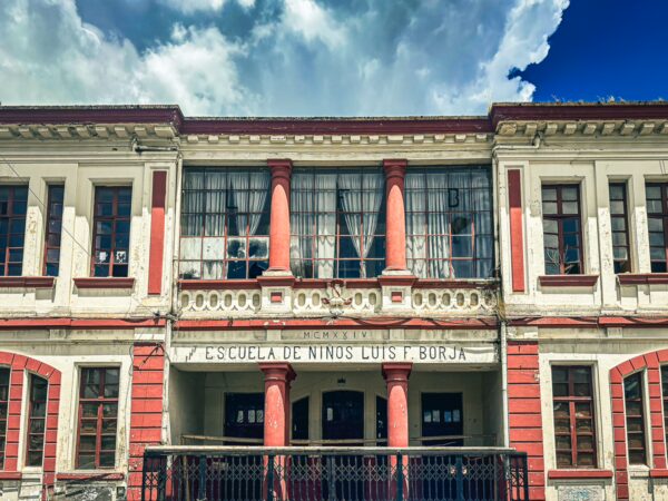 Historic architecture featuring red and white façades with large windows, located in Machachi, Ecuador. Bright clouds fill the sky.