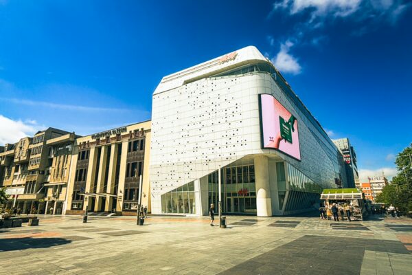 Mercur Center showcases modern architecture with a glass facade in Craiova, Romania, surrounded by historic buildings and blue skies.