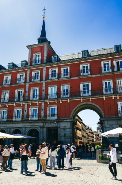 Vibrant Plaza Mayor in Madrid, featuring a lively crowd and stunning red architecture under a clear blue sky.