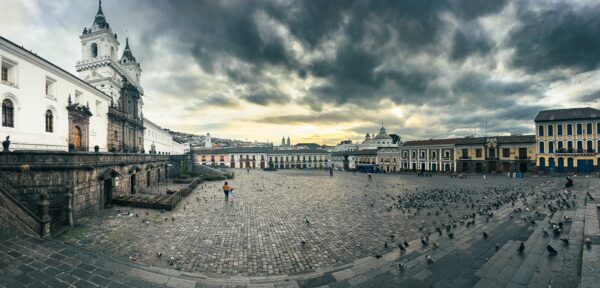 Historic architecture and cobblestone paths in San Francisco Square, Quito, Ecuador, under a dramatic sky at sunset.