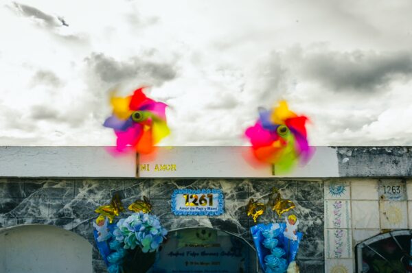 Colorful pinwheels spin above a decorated tomb at Tulcán Cemetery, Ecuador, with vibrant flowers against a cloudy sky.