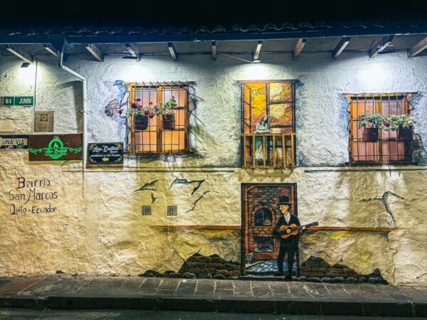 Colorful murals and a musician enhance the vibrant street scene in San Marcos, Quito, Ecuador, showcasing local culture.