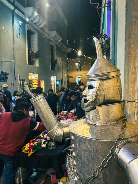 Bronze sculpture greets visitors along Juan de Dios Morales Street, bustling with vendors and festive lights in Quito, Ecuador.