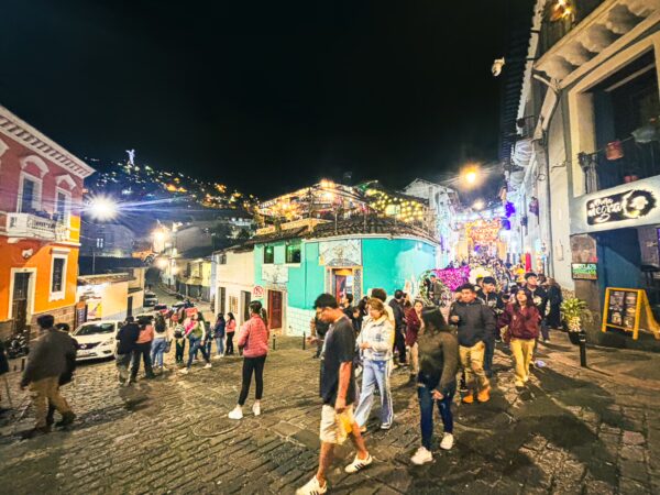 Colorful buildings line Juan de Dios Morales Street in La Ronda, Quito, bustling with visitors under vibrant nighttime lights.