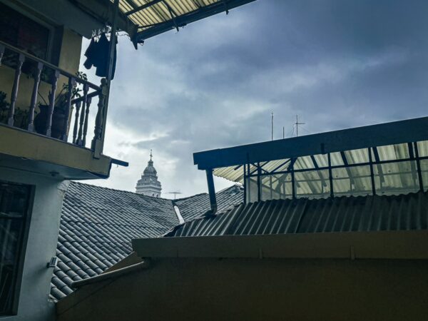 View from Hostal Yumbo shows rooftops under a moody sky, with a distant clock tower peeking through the clouds in Quito, Ecuador.