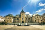 Elegant administrative palace in Craiova, Romania, showcasing intricate architecture, bright blue skies, and decorative fountains.