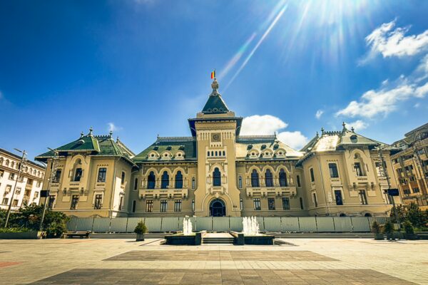 Elegant administrative palace in Craiova, Romania, showcasing intricate architecture, bright blue skies, and decorative fountains.