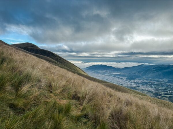 Majestic Imbabura Volcano rises above sweeping green hills and valleys under a cloudy sky in Ecuador, showcasing breathtaking landscapes.