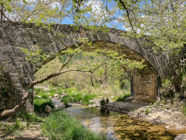Charming stone bridge arches over a clear stream surrounded by lush greenery in Vytina, near Nymfasia, Arcadia, Greece.