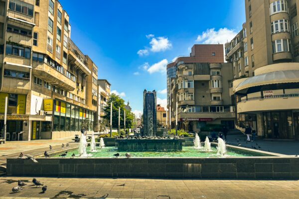 Calea Unirii features a fountain surrounded by modern buildings and a clear blue sky in Craiova, Romania.