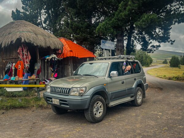 A four-wheel vehicle parked near a colorful roadside shop in Cotopaxi National Park, Ecuador, surrounded by lush greenery.