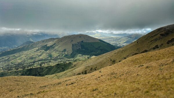 Majestic Imbabura Volcano rises above rolling green hills and golden grasses under a dramatic cloudy sky in Ecuador.
